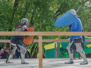 Tver / Rusya - 29 Eylül 2020: Ağır zırhlı savaşçılar kılıçlarla savaşıyor. Arka planda, hakem ve seyirciler. Ortaçağ Avrupa şövalye turnuvalarının tarihi yeniden yapılandırması