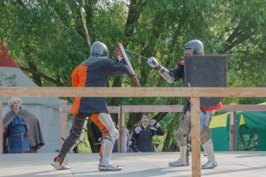 Tver / Rusya - 29 Eylül 2020: Ağır zırhlı savaşçılar kılıçlarla savaşıyor. Arka planda, hakem ve seyirciler. Ortaçağ Avrupa şövalye turnuvalarının tarihi yeniden yapılandırması