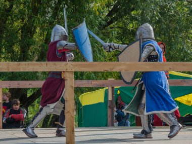 Tver / Rusya - 29 Eylül 2020: Ağır zırhlı savaşçılar kılıçlarla savaşıyor. Arka planda, hakem ve seyirciler. Ortaçağ Avrupa şövalye turnuvalarının tarihi yeniden yapılandırması