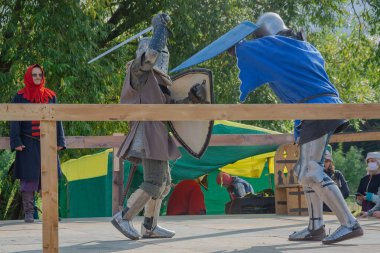 Tver / Rusya - 29 Eylül 2020: Ağır zırhlı savaşçılar kılıçlarla savaşıyor. Arka planda, hakem ve seyirciler. Ortaçağ Avrupa şövalye turnuvalarının tarihi yeniden yapılandırması