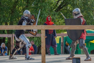 Tver / Rusya - 29 Eylül 2020: Ağır zırhlı savaşçılar kılıçlarla savaşıyor. Arka planda, hakem ve seyirciler. Ortaçağ Avrupa şövalye turnuvalarının tarihi yeniden yapılandırması