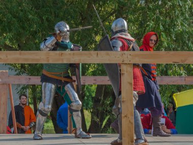 Tver / Rusya - 29 Eylül 2020: Ağır zırhlı savaşçılar kılıçlarla savaşıyor. Arka planda, hakem ve seyirciler. Ortaçağ Avrupa şövalye turnuvalarının tarihi yeniden yapılandırması