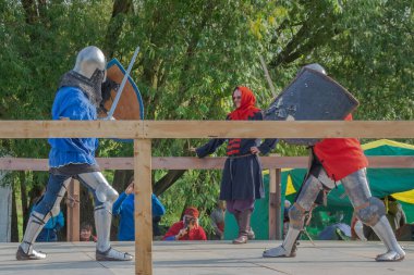 Tver / Rusya - 29 Eylül 2020: Ağır zırhlı savaşçılar kılıçlarla savaşıyor. Arka planda, hakem ve seyirciler. Ortaçağ Avrupa şövalye turnuvalarının tarihi yeniden yapılandırması