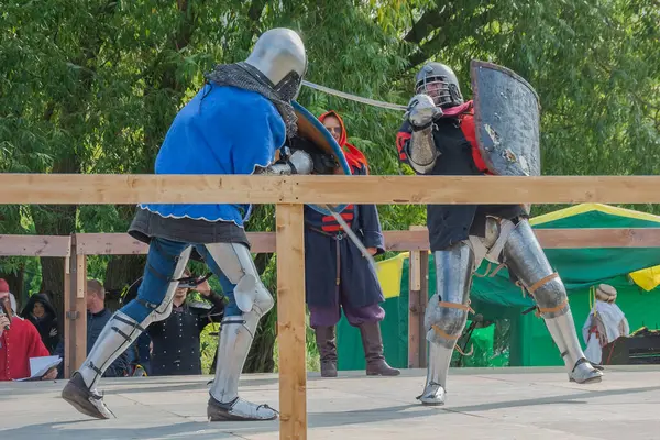 Tver / Rusya - 29 Eylül 2020: Ağır zırhlı savaşçılar kılıçlarla savaşıyor. Arka planda, hakem ve seyirciler. Ortaçağ Avrupa şövalye turnuvalarının tarihi yeniden yapılandırması