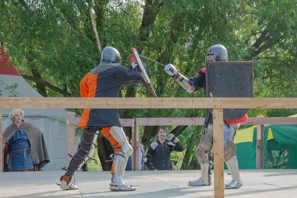Tver / Rusya - 29 Eylül 2020: Ağır zırhlı savaşçılar kılıçlarla savaşıyor. Arka planda, hakem ve seyirciler. Ortaçağ Avrupa şövalye turnuvalarının tarihi yeniden yapılandırması
