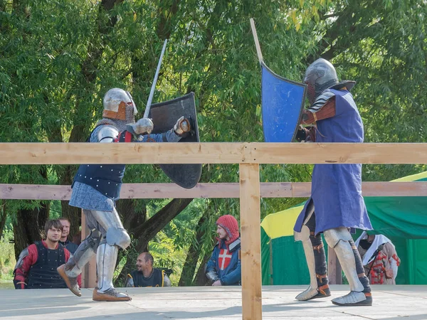 Tver / Rusya - 29 Eylül 2020: Ağır zırhlı savaşçılar kılıçlarla savaşıyor. Arka planda, hakem ve seyirciler. Ortaçağ Avrupa şövalye turnuvalarının tarihi yeniden yapılandırması
