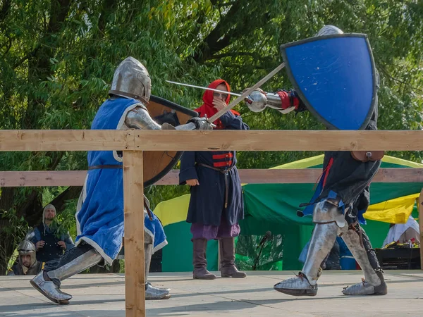 Tver / Rusya - 29 Eylül 2020: Ağır zırhlı savaşçılar kılıçlarla savaşıyor. Arka planda, hakem ve seyirciler. Ortaçağ Avrupa şövalye turnuvalarının tarihi yeniden yapılandırması