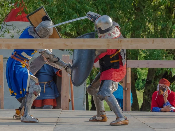 Tver / Rusya - 29 Eylül 2020: Ağır zırhlı savaşçılar kılıçlarla savaşıyor. Arka planda, hakem ve seyirciler. Ortaçağ Avrupa şövalye turnuvalarının tarihi yeniden yapılandırması