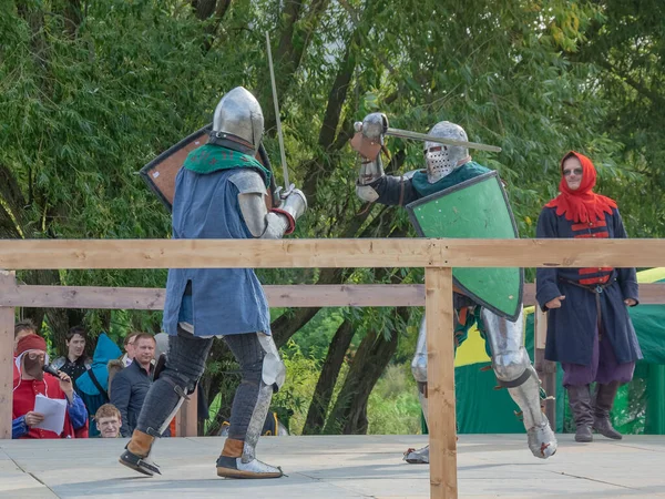 Tver / Rusya - 29 Eylül 2020: Ağır zırhlı savaşçılar kılıçlarla savaşıyor. Arka planda, hakem ve seyirciler. Ortaçağ Avrupa şövalye turnuvalarının tarihi yeniden yapılandırması