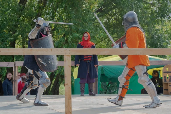 Tver / Rusya - 29 Eylül 2020: Ağır zırhlı savaşçılar kılıçlarla savaşıyor. Arka planda, hakem ve seyirciler. Ortaçağ Avrupa şövalye turnuvalarının tarihi yeniden yapılandırması
