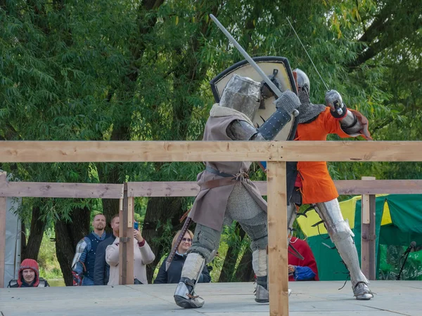 Tver / Rusya - 29 Eylül 2020: Ağır zırhlı savaşçılar kılıçlarla savaşıyor. Arka planda, hakem ve seyirciler. Ortaçağ Avrupa şövalye turnuvalarının tarihi yeniden yapılandırması