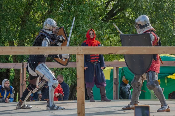 Tver / Rusya - 29 Eylül 2020: Ağır zırhlı savaşçılar kılıçlarla savaşıyor. Arka planda, hakem ve seyirciler. Ortaçağ Avrupa şövalye turnuvalarının tarihi yeniden yapılandırması