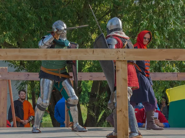 Tver / Rusya - 29 Eylül 2020: Ağır zırhlı savaşçılar kılıçlarla savaşıyor. Arka planda, hakem ve seyirciler. Ortaçağ Avrupa şövalye turnuvalarının tarihi yeniden yapılandırması
