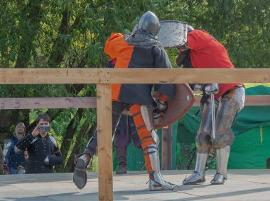 Tver / Rusya - 29 Eylül 2020: Ağır zırhlı savaşçılar kılıçlarla savaşıyor. Arka planda, hakem ve seyirciler. Ortaçağ Avrupa şövalye turnuvalarının tarihi yeniden yapılandırması