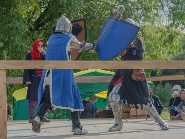 Tver / Rusya - 29 Eylül 2020: Ağır zırhlı savaşçılar kılıçlarla savaşıyor. Arka planda, hakem ve seyirciler. Ortaçağ Avrupa şövalye turnuvalarının tarihi yeniden yapılandırması