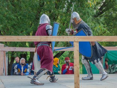 Tver / Rusya - 29 Eylül 2020: Ağır zırhlı savaşçılar kılıçlarla savaşıyor. Arka planda, hakem ve seyirciler. Ortaçağ Avrupa şövalye turnuvalarının tarihi yeniden yapılandırması