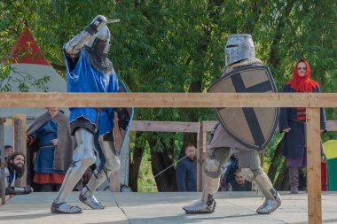 Tver / Rusya - 29 Eylül 2020: Ağır zırhlı savaşçılar kılıçlarla savaşıyor. Arka planda, hakem ve seyirciler. Ortaçağ Avrupa şövalye turnuvalarının tarihi yeniden yapılandırması