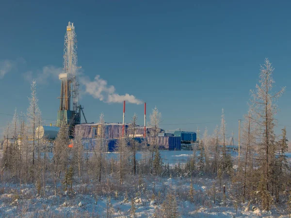 Drilling oil and gas wells in the northern field. Polar frosty day. Winter forest-tundra landscape in the snow with a drilling rig. Beautiful sky