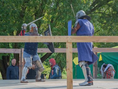 Tver / Rusya - 29 Eylül 2020: Ağır zırhlı savaşçılar kılıçlarla savaşıyor. Arka planda, hakem ve seyirciler. Ortaçağ Avrupa şövalye turnuvalarının tarihi yeniden yapılandırması