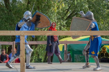 Tver / Rusya - 29 Eylül 2020: Ağır zırhlı savaşçılar kılıçlarla savaşıyor. Arka planda, hakem ve seyirciler. Ortaçağ Avrupa şövalye turnuvalarının tarihi yeniden yapılandırması