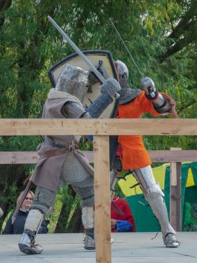 Tver / Rusya - 29 Eylül 2020: Ağır zırhlı savaşçılar kılıçlarla savaşıyor. Arka planda, hakem ve seyirciler. Ortaçağ Avrupa şövalye turnuvalarının tarihi yeniden yapılandırması