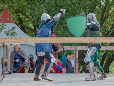 Tver / Rusya - 29 Eylül 2020: Ağır zırhlı savaşçılar kılıçlarla savaşıyor. Arka planda, hakem ve seyirciler. Ortaçağ Avrupa şövalye turnuvalarının tarihi yeniden yapılandırması