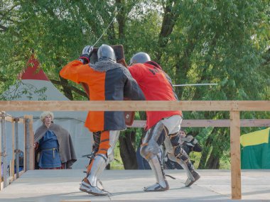 Tver / Rusya - 29 Eylül 2020: Ağır zırhlı savaşçılar kılıçlarla savaşıyor. Arka planda, hakem ve seyirciler. Ortaçağ Avrupa şövalye turnuvalarının tarihi yeniden yapılandırması