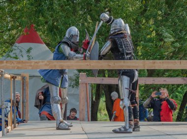 Tver / Rusya - 29 Eylül 2020: Ağır zırhlı savaşçılar kılıçlarla savaşıyor. Arka planda, hakem ve seyirciler. Ortaçağ Avrupa şövalye turnuvalarının tarihi yeniden yapılandırması