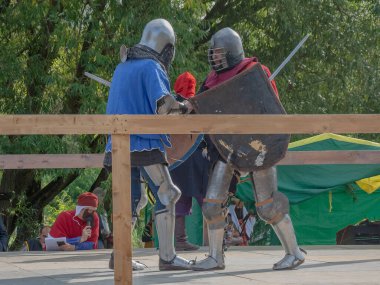 Tver / Rusya - 29 Eylül 2020: Ağır zırhlı savaşçılar kılıçlarla savaşıyor. Arka planda, hakem ve seyirciler. Ortaçağ Avrupa şövalye turnuvalarının tarihi yeniden yapılandırması