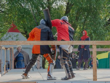 Tver / Rusya - 29 Eylül 2020: Ağır zırhlı savaşçılar kılıçlarla savaşıyor. Arka planda, hakem ve seyirciler. Ortaçağ Avrupa şövalye turnuvalarının tarihi yeniden yapılandırması