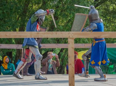 Tver / Rusya - 29 Eylül 2020: Ağır zırhlı savaşçılar kılıçlarla savaşıyor. Arka planda, hakem ve seyirciler. Ortaçağ Avrupa şövalye turnuvalarının tarihi yeniden yapılandırması