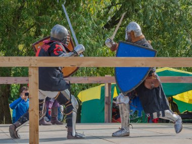 Tver / Rusya - 29 Eylül 2020: Ağır zırhlı savaşçılar kılıçlarla savaşıyor. Arka planda, hakem ve seyirciler. Ortaçağ Avrupa şövalye turnuvalarının tarihi yeniden yapılandırması