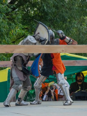 Tver / Rusya - 29 Eylül 2020: Ağır zırhlı savaşçılar kılıçlarla savaşıyor. Arka planda, hakem ve seyirciler. Ortaçağ Avrupa şövalye turnuvalarının tarihi yeniden yapılandırması