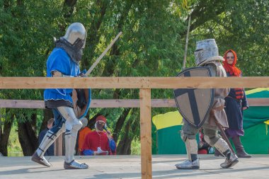 Tver / Rusya - 29 Eylül 2020: Ağır zırhlı savaşçılar kılıçlarla savaşıyor. Arka planda, hakem ve seyirciler. Ortaçağ Avrupa şövalye turnuvalarının tarihi yeniden yapılandırması