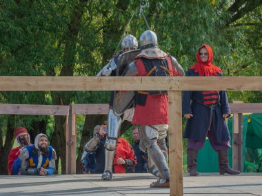 Tver / Rusya - 29 Eylül 2020: Ağır zırhlı savaşçılar kılıçlarla savaşıyor. Arka planda, hakem ve seyirciler. Ortaçağ Avrupa şövalye turnuvalarının tarihi yeniden yapılandırması