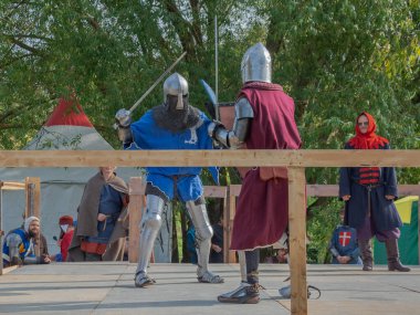 Tver / Rusya - 29 Eylül 2020: Ağır zırhlı savaşçılar kılıçlarla savaşıyor. Arka planda, hakem ve seyirciler. Ortaçağ Avrupa şövalye turnuvalarının tarihi yeniden yapılandırması