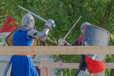 Tver / Rusya - 29 Eylül 2020: Ağır zırhlı savaşçılar kılıçlarla savaşıyor. Arka planda, hakem ve seyirciler. Ortaçağ Avrupa şövalye turnuvalarının tarihi yeniden yapılandırması