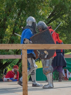 Tver / Rusya - 29 Eylül 2020: Ağır zırhlı savaşçılar kılıçlarla savaşıyor. Arka planda, hakem ve seyirciler. Ortaçağ Avrupa şövalye turnuvalarının tarihi yeniden yapılandırması