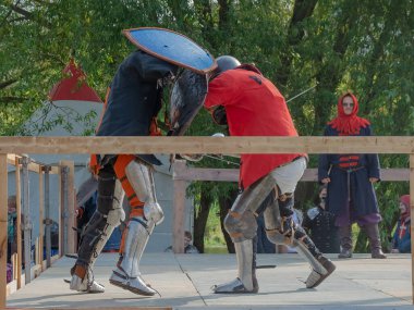 Tver / Rusya - 29 Eylül 2020: Ağır zırhlı savaşçılar kılıçlarla savaşıyor. Arka planda, hakem ve seyirciler. Ortaçağ Avrupa şövalye turnuvalarının tarihi yeniden yapılandırması