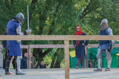 Tver / Rusya - 29 Eylül 2020: Ağır zırhlı savaşçılar kılıçlarla savaşıyor. Arka planda, hakem ve seyirciler. Ortaçağ Avrupa şövalye turnuvalarının tarihi yeniden yapılandırması