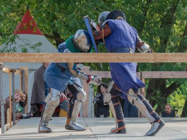 Tver / Rusya - 29 Eylül 2020: Ağır zırhlı savaşçılar kılıçlarla savaşıyor. Arka planda, hakem ve seyirciler. Ortaçağ Avrupa şövalye turnuvalarının tarihi yeniden yapılandırması