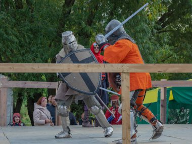 Tver / Rusya - 29 Eylül 2020: Ağır zırhlı savaşçılar kılıçlarla savaşıyor. Arka planda, hakem ve seyirciler. Ortaçağ Avrupa şövalye turnuvalarının tarihi yeniden yapılandırması