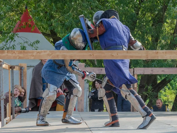Tver / Rusya - 29 Eylül 2020: Ağır zırhlı savaşçılar kılıçlarla savaşıyor. Arka planda, hakem ve seyirciler. Ortaçağ Avrupa şövalye turnuvalarının tarihi yeniden yapılandırması