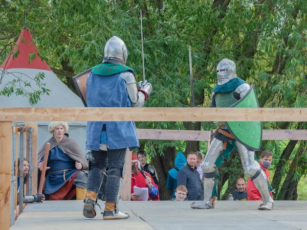 Tver / Rusya - 29 Eylül 2020: Ağır zırhlı savaşçılar kılıçlarla savaşıyor. Arka planda, hakem ve seyirciler. Ortaçağ Avrupa şövalye turnuvalarının tarihi yeniden yapılandırması