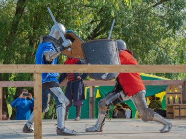 Tver / Rusya - 29 Eylül 2020: Ağır zırhlı savaşçılar kılıçlarla savaşıyor. Arka planda, hakem ve seyirciler. Ortaçağ Avrupa şövalye turnuvalarının tarihi yeniden yapılandırması