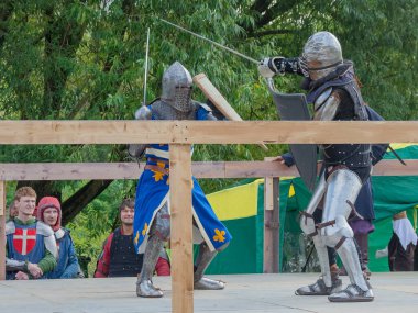 Tver / Rusya - 29 Eylül 2020: Ağır zırhlı savaşçılar kılıçlarla savaşıyor. Arka planda, hakem ve seyirciler. Ortaçağ Avrupa şövalye turnuvalarının tarihi yeniden yapılandırması