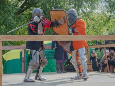 Tver / Rusya - 29 Eylül 2020: Ağır zırhlı savaşçılar kılıçlarla savaşıyor. Arka planda, hakem ve seyirciler. Ortaçağ Avrupa şövalye turnuvalarının tarihi yeniden yapılandırması