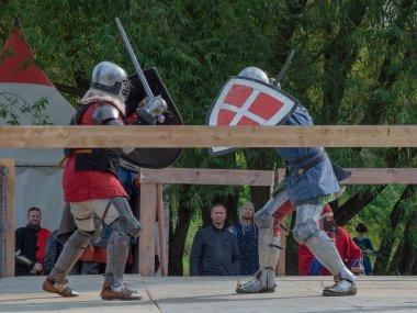 Tver / Rusya - 29 Eylül 2020: Ağır zırhlı savaşçılar kılıçlarla savaşıyor. Arka planda, hakem ve seyirciler. Ortaçağ Avrupa şövalye turnuvalarının tarihi yeniden yapılandırması