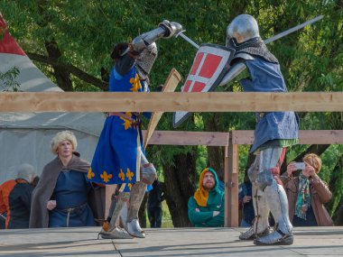 Tver / Rusya - 29 Eylül 2020: Ağır zırhlı savaşçılar kılıçlarla savaşıyor. Arka planda, hakem ve seyirciler. Ortaçağ Avrupa şövalye turnuvalarının tarihi yeniden yapılandırması