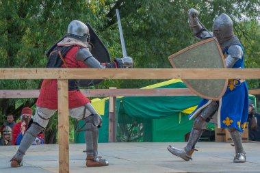 Tver / Rusya - 29 Eylül 2020: Ağır zırhlı savaşçılar kılıçlarla savaşıyor. Arka planda, hakem ve seyirciler. Ortaçağ Avrupa şövalye turnuvalarının tarihi yeniden yapılandırması